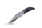 Two Damascus pattern folding knives with curved silver-gray patterned blades, copper-colored accents, ornate pivot fittings, and brown and black handles