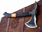 Norse Rune Viking Axe with blackened textured metal head, pointed projection, curved silver-edged blade, rune-style markings and dark wood-look handle with orange symbols.