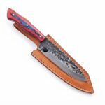Red and blue chef knife with three silver-tone handle pins and a two-tone blade resting diagonally across a tan stitched sheath.