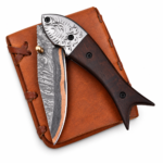 Engraved Bolster Damascus Folding Knife with patterned curved blade, copper-colored accent, dark brown wood-look handle and embossed brown carrying pouch.