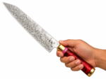 Damascus Steel Chef Knife with long wave-patterned blade, glossy ruby-red handle, pink decorative spacer, and gold-colored metal fittings.