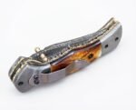Damascus Folding Pocket Knife with silver-gray patterned blade, amber-brown handle, decorative metal bolsters and thumb stud