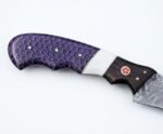 Purple honeycomb fillet knife with a slender gray patterned blade, segmented dark handle, pale divider, and decorative pin beside a brown stitched sheath.