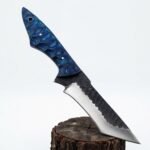 Blue Scalloped Handle Fixed Blade Knife with dark-and-silver curved blade, tapered patterned grip and reddish-brown embossed sheath displayed against a small log.