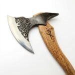 Spiked Viking style axe with a bright crescent blade, circular decoration on a dark head, curved brown grain-look handle, and dark loop.