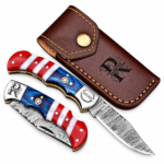 Open red white and blue folding knife with a patterned blade, star handle detail and monogrammed silver-tone bolster resting on a brown stitched pouch.