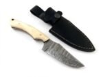 Ivory Handle Curved Skinner Knife with silver-gray Damascus-style patterned blade, cream-colored contoured handle and black stitched leather-style sheath.