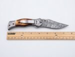 Damascus Folding Pocket Knife with silver-gray patterned blade, amber-brown handle, decorative metal bolsters and thumb stud