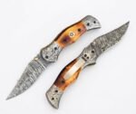 Damascus Folding Pocket Knife with silver-gray patterned blade, amber-brown handle, decorative metal bolsters and thumb stud