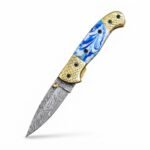 Blue Marble Damascus Folding Knife shown open with silver-gray patterned blade, blue-and-white marbled handle and gold-tone grid-patterned bolsters
