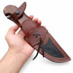 Brown handle Bowie knife held in a hand, showing a broad gray patterned blade, matching curved guard, hooked grain-look grip, and silver-tone pin.