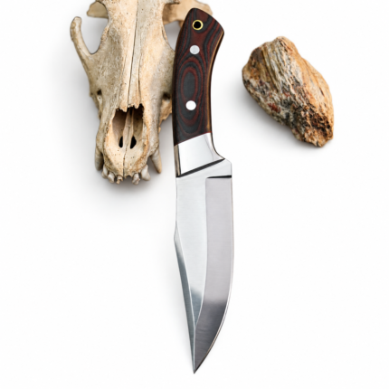 Red and black fixed blade knife with two silver-tone handle pins, a gold-tone lanyard hole, and reflective bolster beside an animal skull