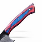 Red and blue chef knife with three silver-tone handle pins and a two-tone blade resting diagonally across a tan stitched sheath.