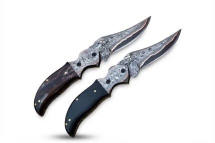 Two Damascus pattern folding knives with curved silver-gray patterned blades, copper-colored accents, ornate pivot fittings, and brown and black handles