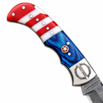 Open red white and blue folding knife with a patterned blade, star handle detail and monogrammed silver-tone bolster resting on a brown stitched pouch.
