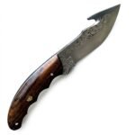 Engraved Fixed Blade Skinning Knife with curved polished blade, ornamental scrollwork, dark brown wood-grain handle and stitched brown sheath