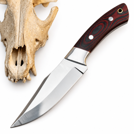 Red and black fixed blade knife with two silver-tone handle pins, a gold-tone lanyard hole, and reflective bolster beside an animal skull