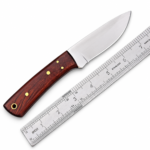 Fixed blade knife with a reddish-brown wood-grain handle, four gold-tone pins, and a lanyard hole beside a metal ruler.