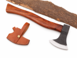 Curved handle hatchet with brown wood-grain handle, dark textured metallic head, bright silver-colored blade edge and tan stitched sheath displayed over natural bark.