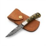 Basket weave handle folding knife with a gray patterned blade, silver-tone bolster, and black-and-gold handle resting across a brown snap-fastened pouch.