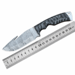 Damascus gut hook hunting knife with black textured handle shown beside measuring ruler