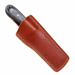 Premium cowboy knife with straight satin-finished blade, circular blade opening, textured black wood-grain handle, silver metal pins, and gold-tone lanyard hole