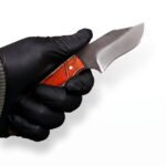 Compact Curved Skinner Knife with broad two-tone blade, brown and cream wood-grain-style handle and tan stitched belt sheath with snap closure.