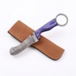 Purple handle ring-pommel knife displayed diagonally over a tan-brown stitched sheath against a white background.