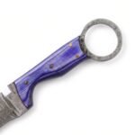 Close-up of violet-purple textured knife handle with four gold-colored pins and a silver-gray ring featuring concentric decorative patterns.