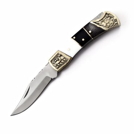 Ornate engraved bolster folding pocket knife with curved silver-colored blade, gold-tone floral fittings, and black and white handle.