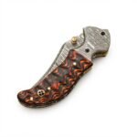 Wavy Handle Damascus Folding Knife with curved patterned blade, black and copper-brown sculpted handle, ornate silver pivot and brown snap-closure pouch.