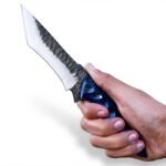 Blue Scalloped Handle Fixed Blade Knife with dark-and-silver curved blade, tapered patterned grip and reddish-brown embossed sheath displayed against a small log.