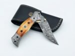 Damascus Folding Pocket Knife with silver-gray patterned blade, amber-brown handle, decorative metal bolsters and thumb stud