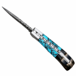 Turquoise pattern handle knife with a Damascus-style blade, black rear handle, and silver-tone bolster resting across a stitched brown sheath.