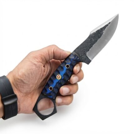 Blue ring pommel skinner knife with dark and silver pointed blade, blue-black patterned handle, mosaic-style pin and large circular rear ring, displayed against a log.