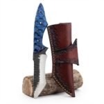 Blue Scalloped Handle Fixed Blade Knife with dark-and-silver curved blade, tapered patterned grip and reddish-brown embossed sheath displayed against a small log.