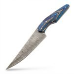 Blue handle trailing point knife with a gray patterned blade, four silver-tone pins, and a curved blue-and-gray grip resting across a black stitched sheath.