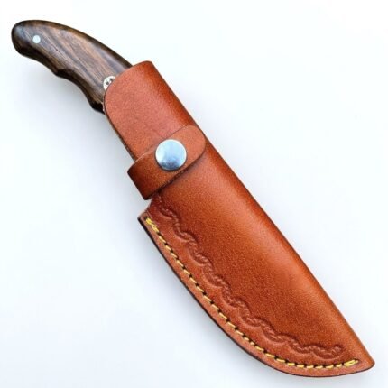 Engraved Fixed Blade Skinning Knife with curved polished blade, ornamental scrollwork, dark brown wood-grain handle and stitched brown sheath