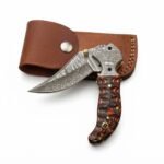 Wavy Handle Damascus Folding Knife with curved patterned blade, black and copper-brown sculpted handle, ornate silver pivot and brown snap-closure pouch.