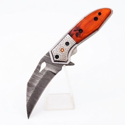 Open orange handle folding knife with a curved patterned blade, elongated blade cutout, and dimpled silver-tone bolster with a star emblem.