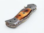 Damascus Folding Pocket Knife with silver-gray patterned blade, amber-brown handle, decorative metal bolsters and thumb stud