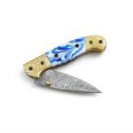 Blue Marble Damascus Folding Knife shown open with silver-gray patterned blade, blue-and-white marbled handle and gold-tone grid-patterned bolsters