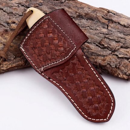 Cream handle Damascus mini cleaver knife with broad wavy-patterned blade, turquoise-blue spacer, silver bolster and brown wrist loop resting against tree bark.