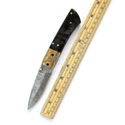 Decorative Spine Folding Pocket Knife photographed from the side in a black-gloved hand, showing intricate silver-colored cutout-style metalwork, a dark handle and a slim pointed blade.