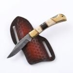 Damascus Pattern Belt Knife with a pointed silver-gray patterned blade, cream-and-black segmented handle, gold-tone fittings and brown basket-weave sheath.
