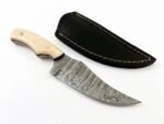 Ivory Handle Curved Skinner Knife with silver-gray Damascus-style patterned blade, cream-colored contoured handle and black stitched leather-style sheath.