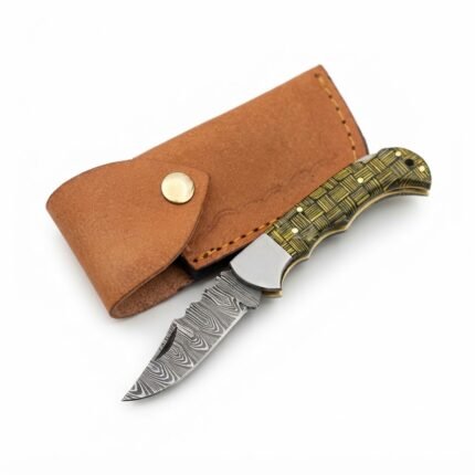 Basket weave handle folding knife with a gray patterned blade, silver-tone bolster, and black-and-gold handle resting across a brown snap-fastened pouch.