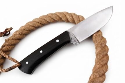 Black handle fixed blade knife with a reflective silver blade, three silver-tone pins, and braided tan lanyard resting over a patterned brown sheath.