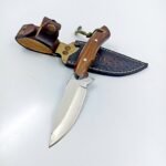Fixed Blade Hunting Knife with polished silver blade, brown wooden handle, green cord lanyard, and decorative brown leather-style sheath