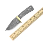Raindrop-pattern knife blank with guard in gold tone, exposed full tang, two small holes, and a larger rear opening beside an inch-and-centimeter ruler